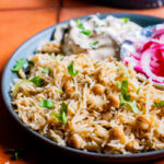 a plate of chana pulao with raita and pickled onions