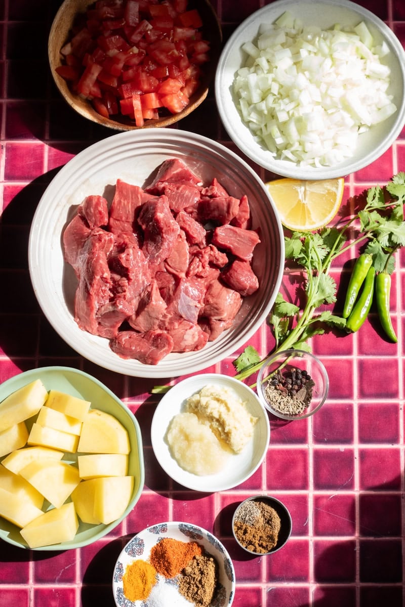 Ingredients for Aaloo Gosht: Stewing beef, chopped tomatoes, ginger and garlic paste, potatoes, spices, chilies, cilantro, lemon, yoghurt.