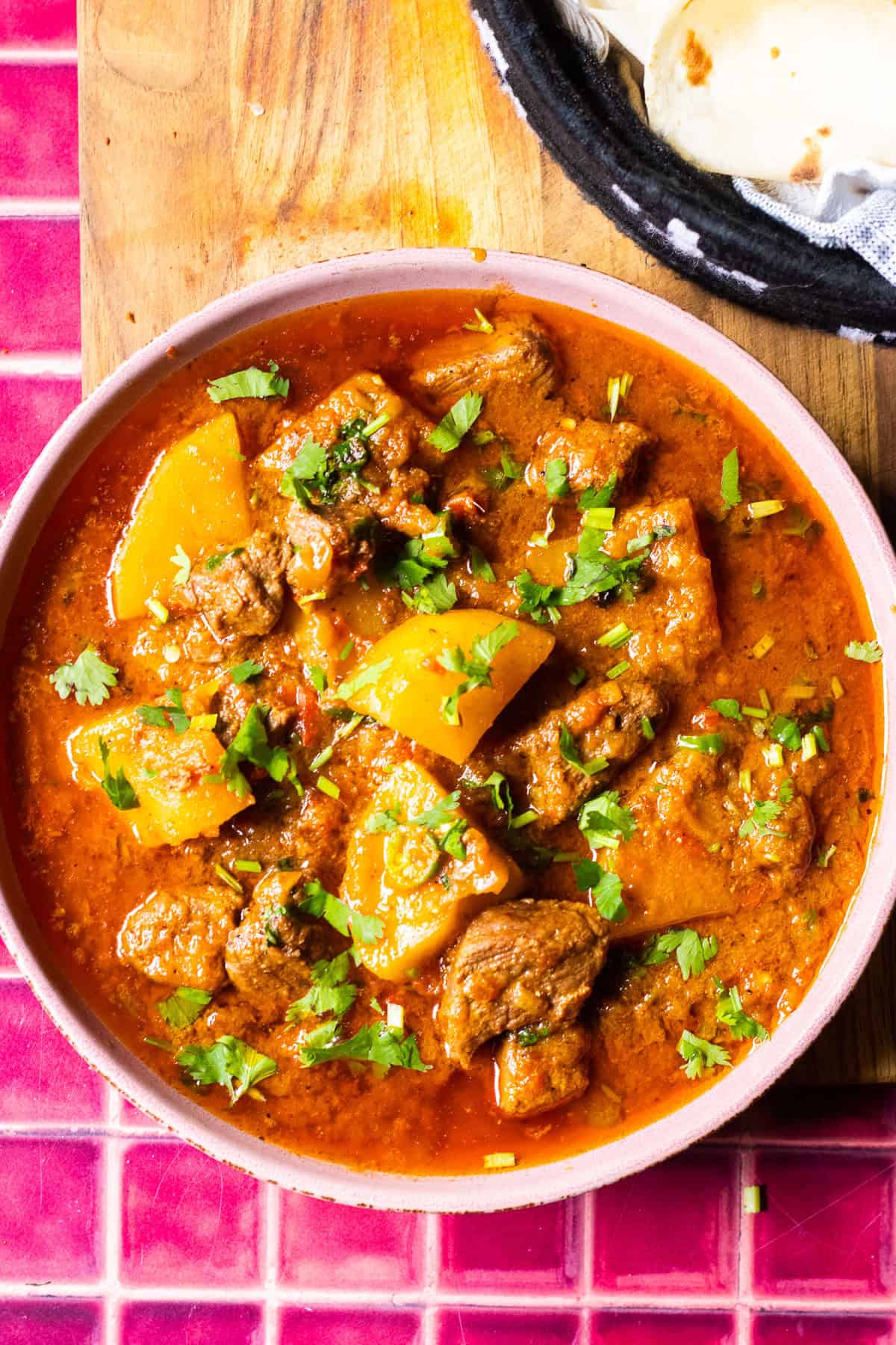 A dish of aloo gosht on a cutting board, Aloo gosht is garnished with cilantro, chilies.