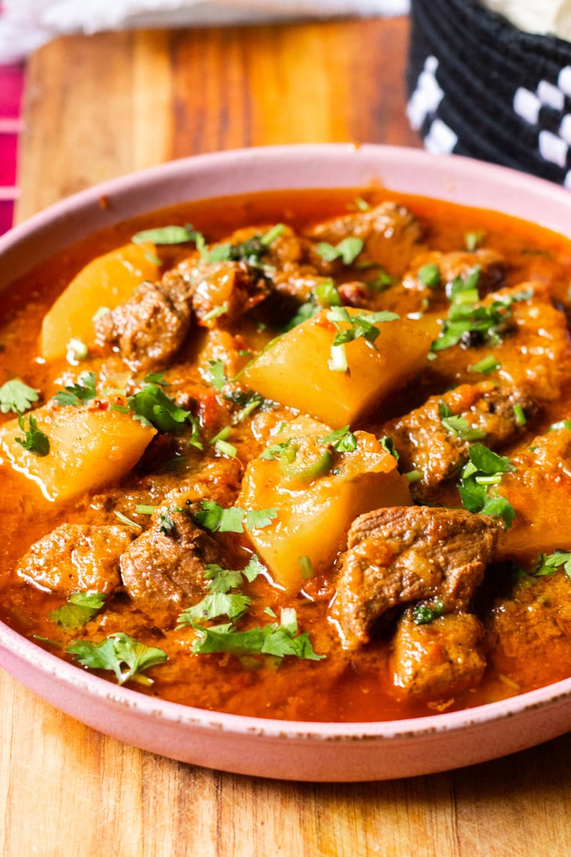 A dish of Aloo gosht garnished with cilantro and green chilies.