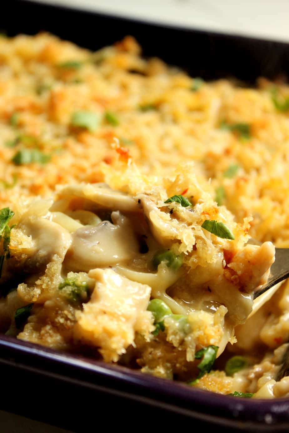 A close-up of creamy Chicken Tetrazzini for Four, featuring chicken, peas, mushrooms, and a golden breadcrumb topping, served from a baking dish with a spoon.