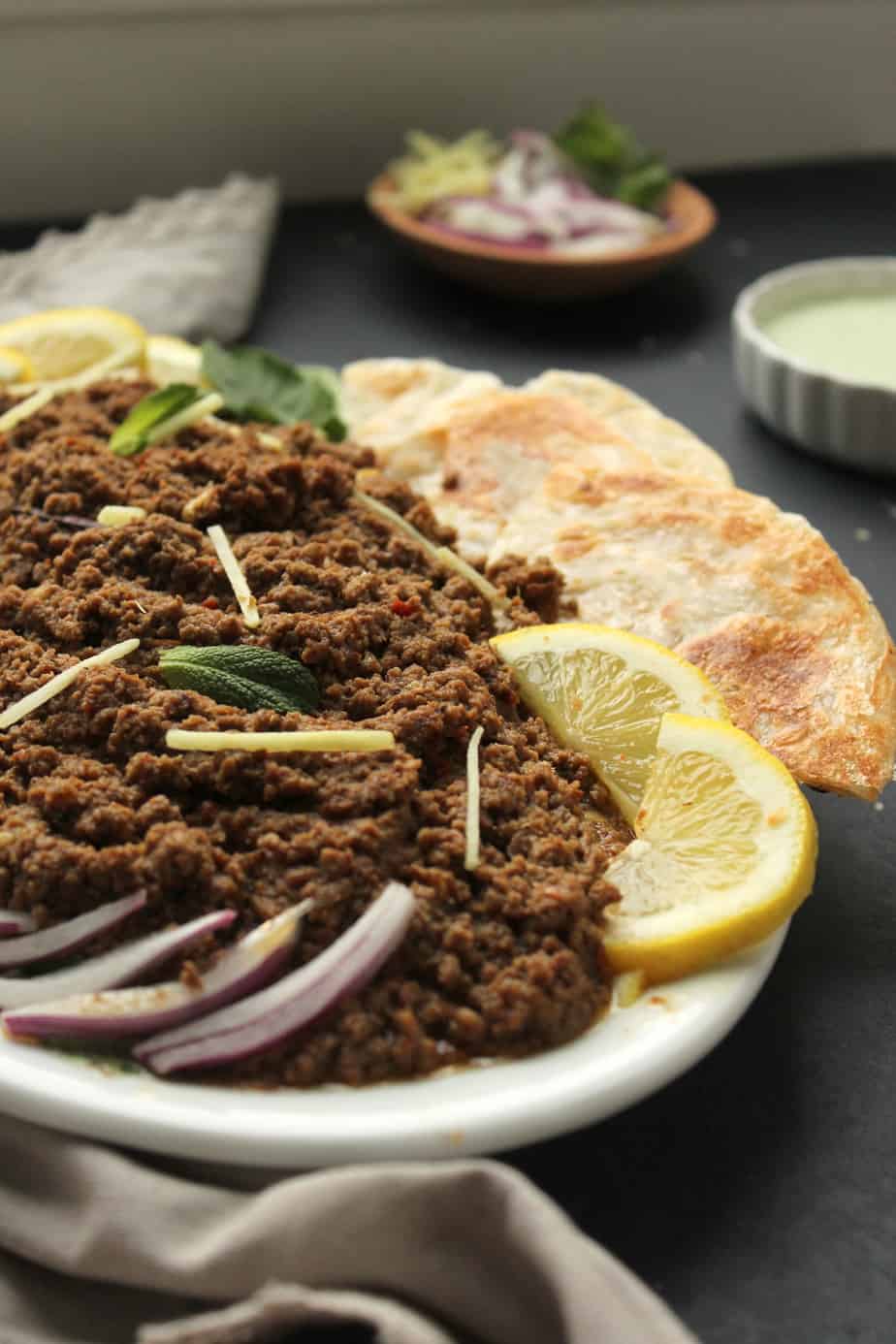 dum ka keema with sliced red onions, mint, and ginger and lemon wedges. paratha on the plate