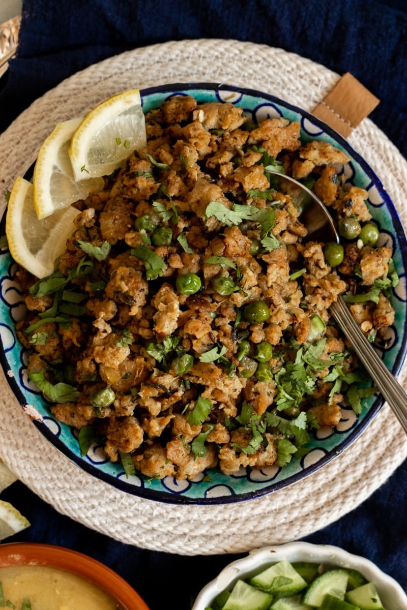 Top down view of a bowl of chicken keema garnished with cilantro and pieces of lemon.