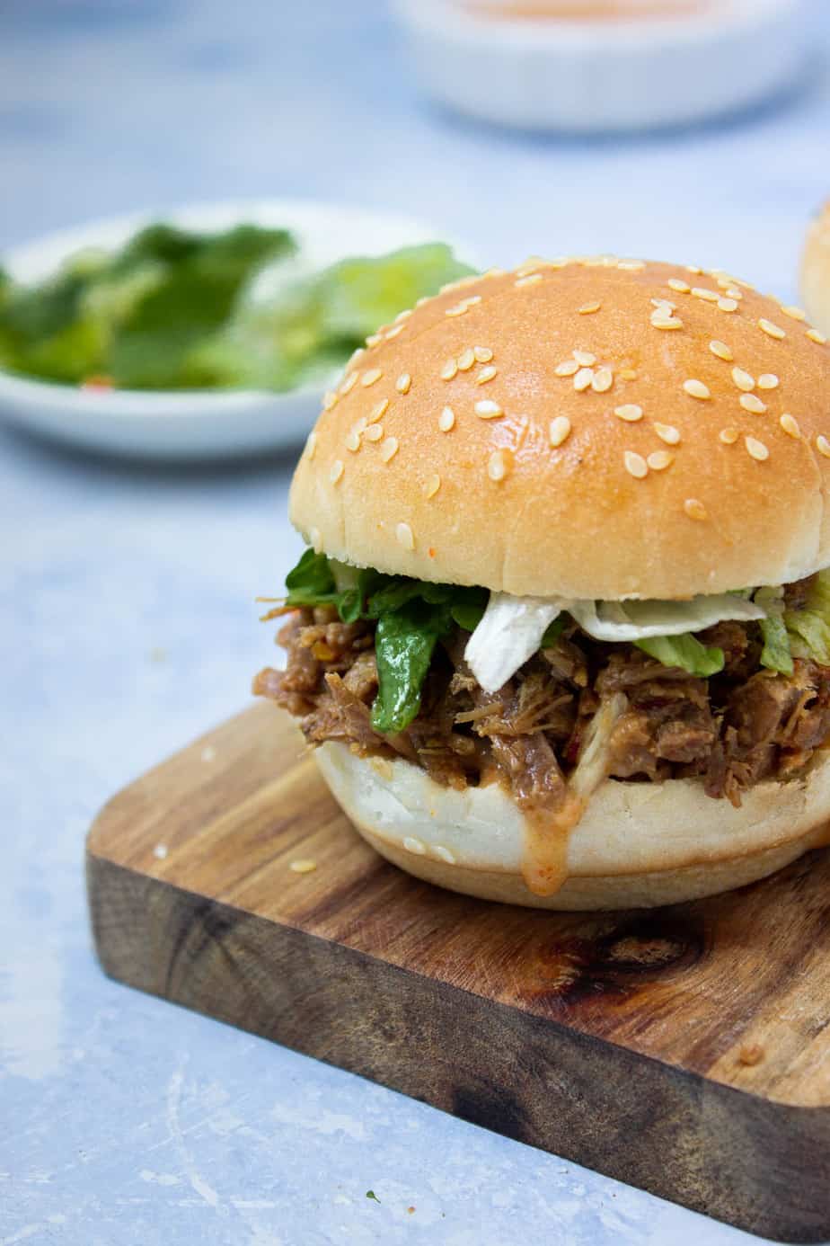 most of a pulled beef slider with lettuce, sauce and some extra greens in the background