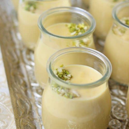 Small glass jars filled with creamy yellow Bread Kheer custard, topped with chopped pistachios, arranged neatly on an ornate silver tray.