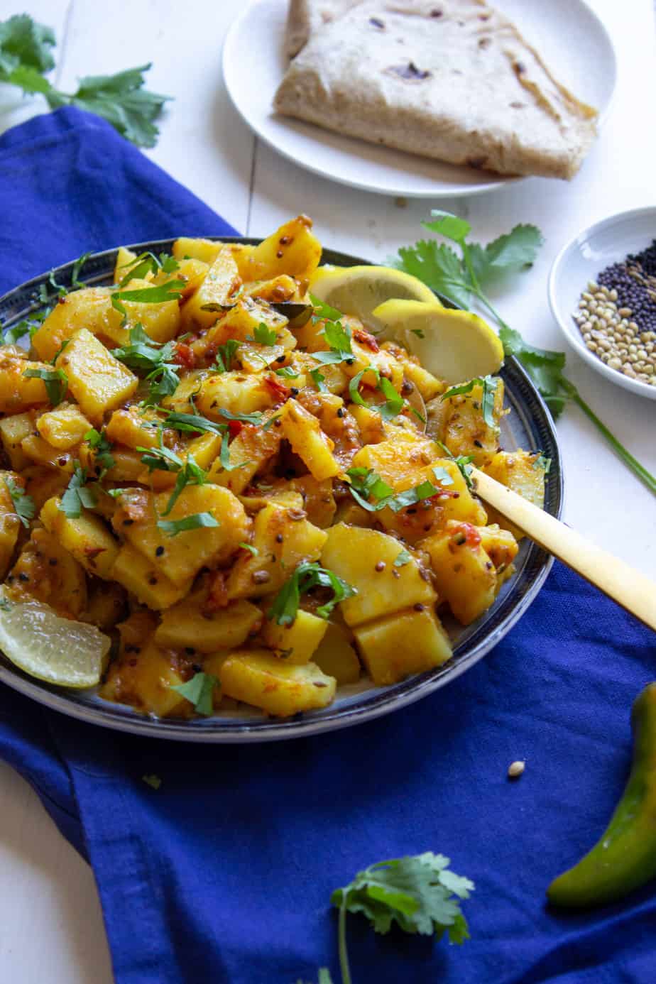 a picture of a plate of achari aloo with roti, a little cilantro and some of the spices showing