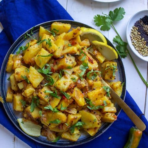A top down shot of a plate of achari aloo, roti in the corner