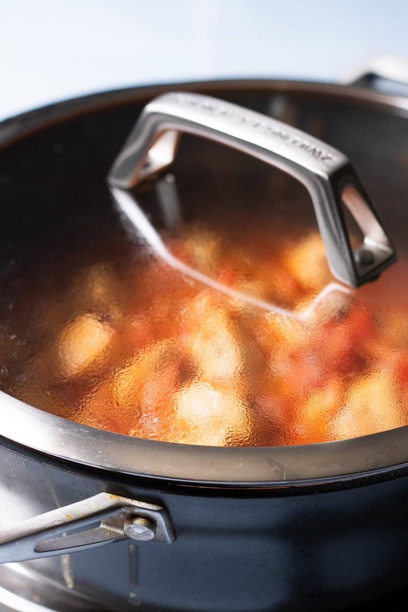 simmering chicken masala covered till tender in a black pot with the lid on