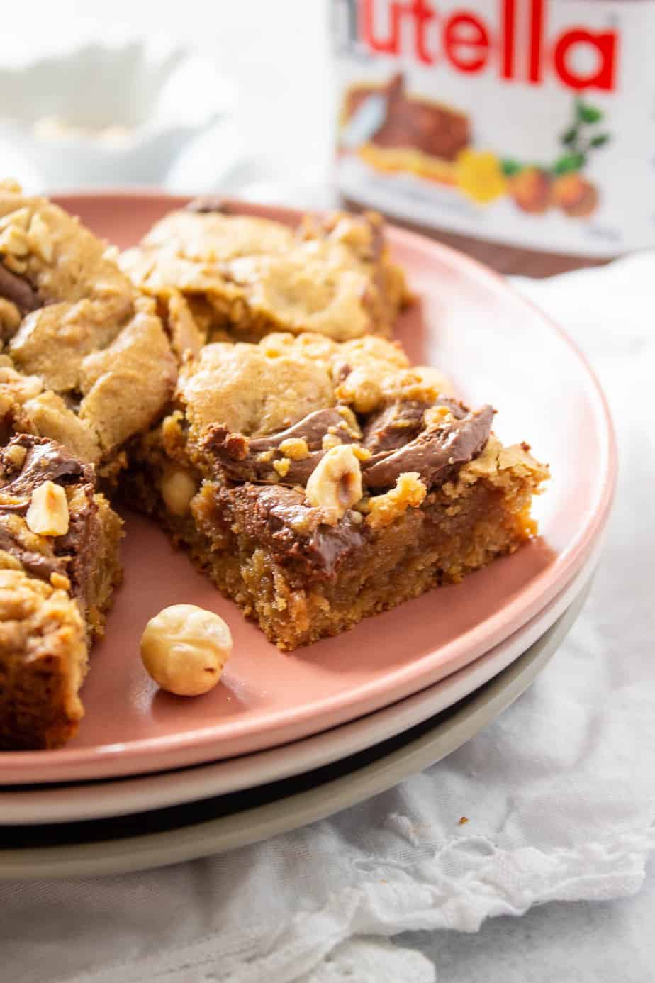Nutella Blondies on a stack of 3 plates with a partial bottle of Nutella in the background