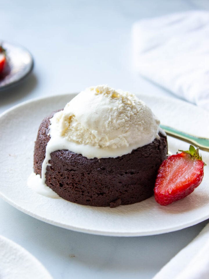 A plate with a lava cake, half a strawberry and melting vanilla ice cream