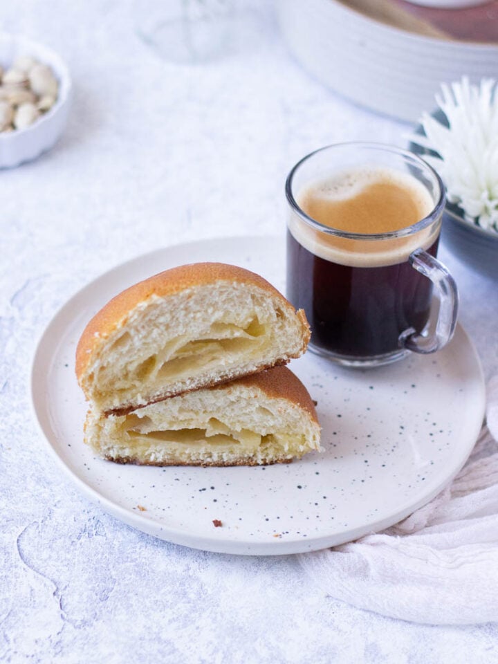 Papaproti Bun halved and on a plate with a cup of coffee. Melted butter centre.