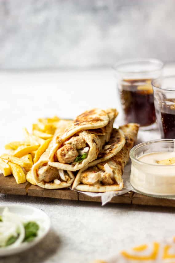 3 boti rolls stacked together, garlic mayo on the side, fries in the frame along with glasses of coke in the background
