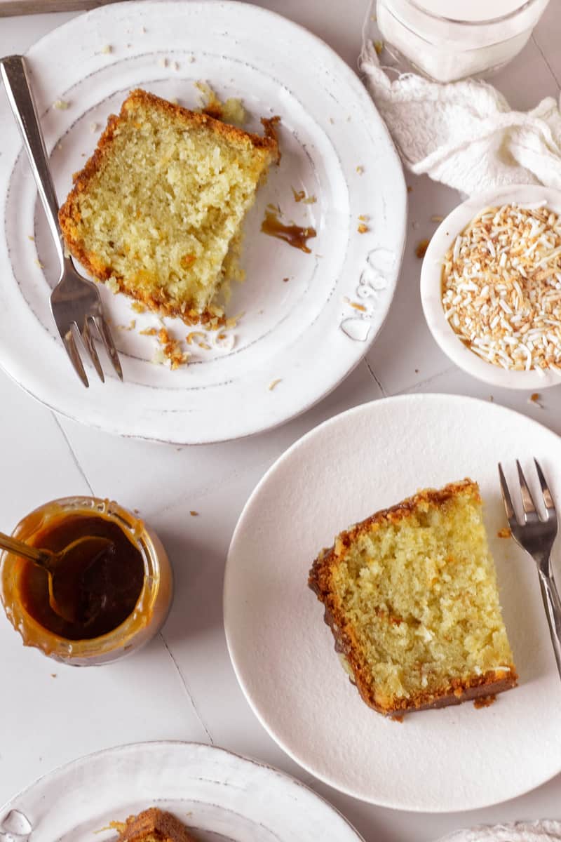 two pieces of coconut loaf cake, a jar of caramel sauce and a bowl of toasted coconut