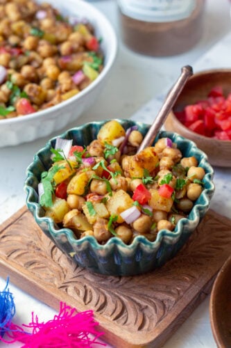 a green bowl of chana chaat on a carved chopping board with a spoon in it