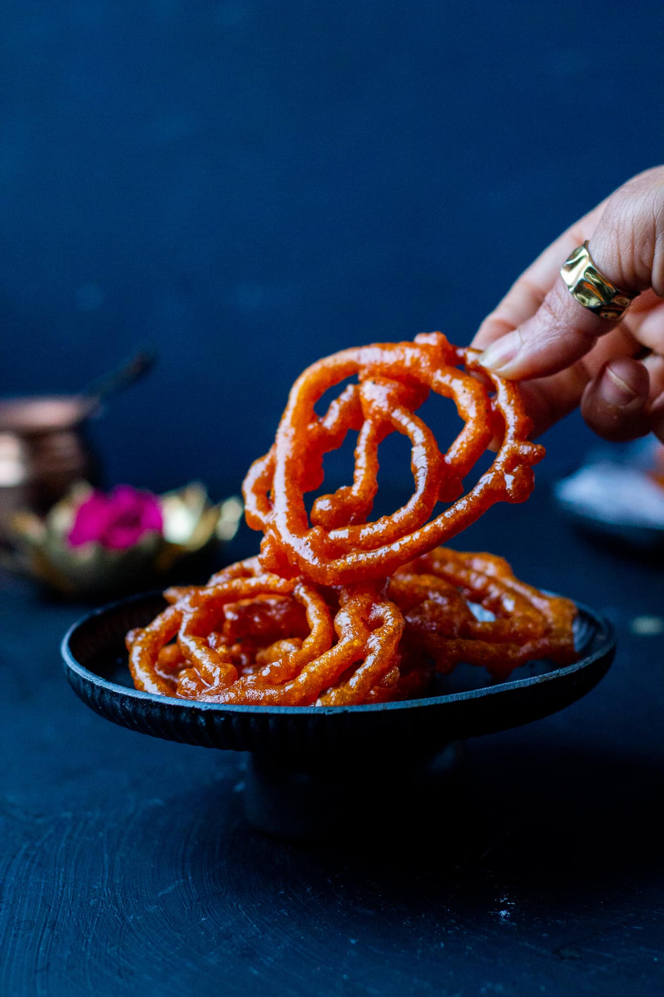 a hand picking up jalebi from a dish