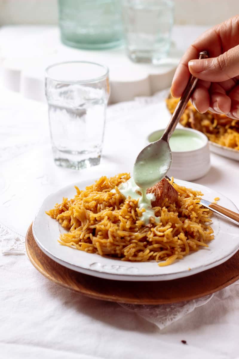 Plate of pakistani chicken pulao with raita drizzled over top