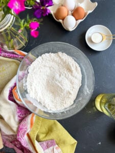 a bowl of whisked dry ingredients surrounded by fabric, flowers and eggs.