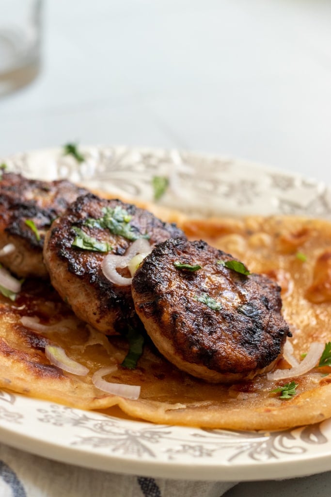 three chicken kababs on top of a paratha with onions scattered over