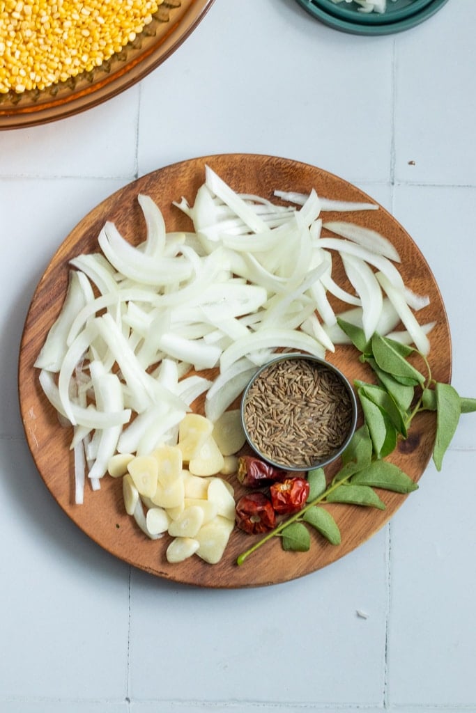 top down view of baghaar ingredients: onions, curry leaves, whole dried red chillies, cumin seeds, and garlic.