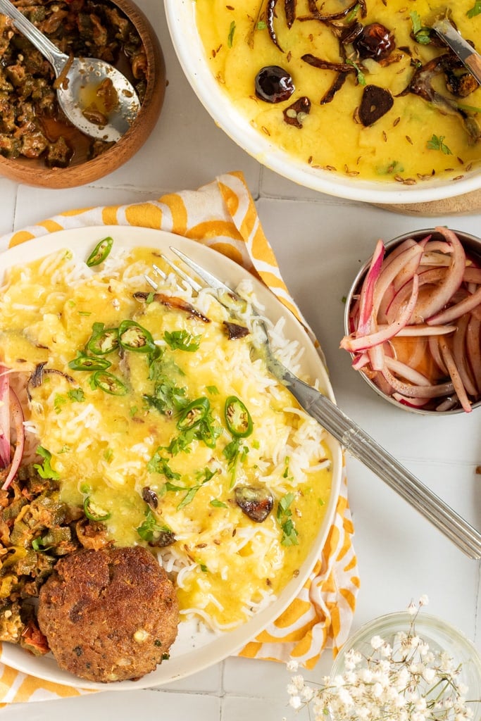 top down view of a plate of daal chawal with crunchy onions, a bowl of bhindi masala, a bowl of daal, some sliced onions