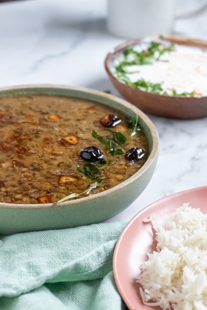 A bowl of sabut masoor on the left middle, rice in the front right, raita in the back right
