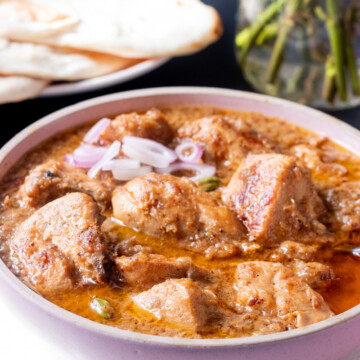 Chicken Korma in a bowl garnished with onions, naan in the background