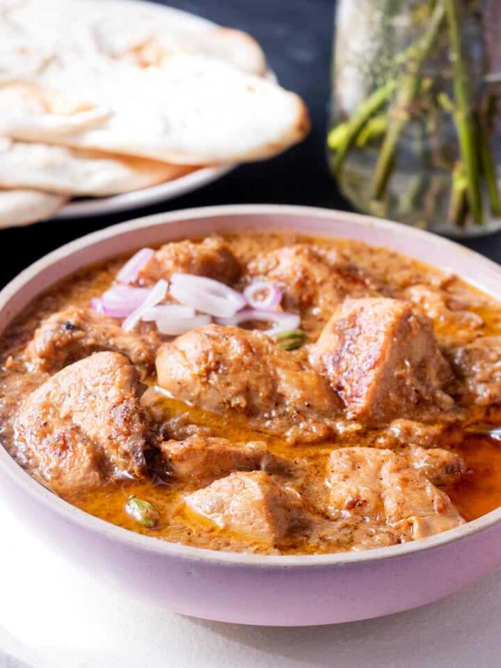 Chicken Korma in a bowl garnished with onions, naan in the background