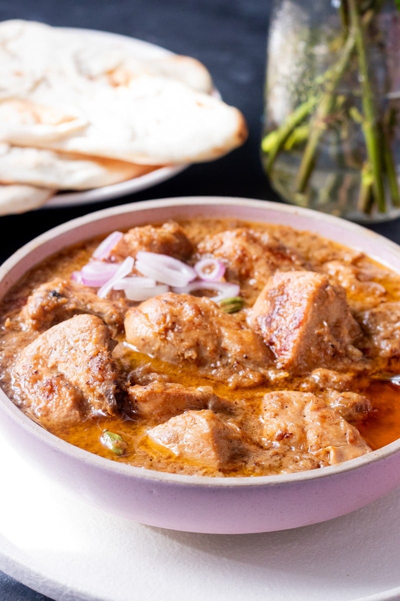 Chicken Korma in a bowl garnished with onions, naan in the background