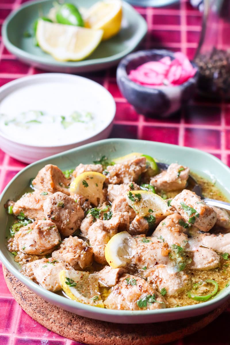 lemon pepper chicken or Murgh Kali Mirch in a green dish, raita, onions and lemons in the background