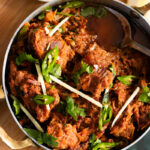 Karahi Gosht top down view with a bowl of ginger in the corner