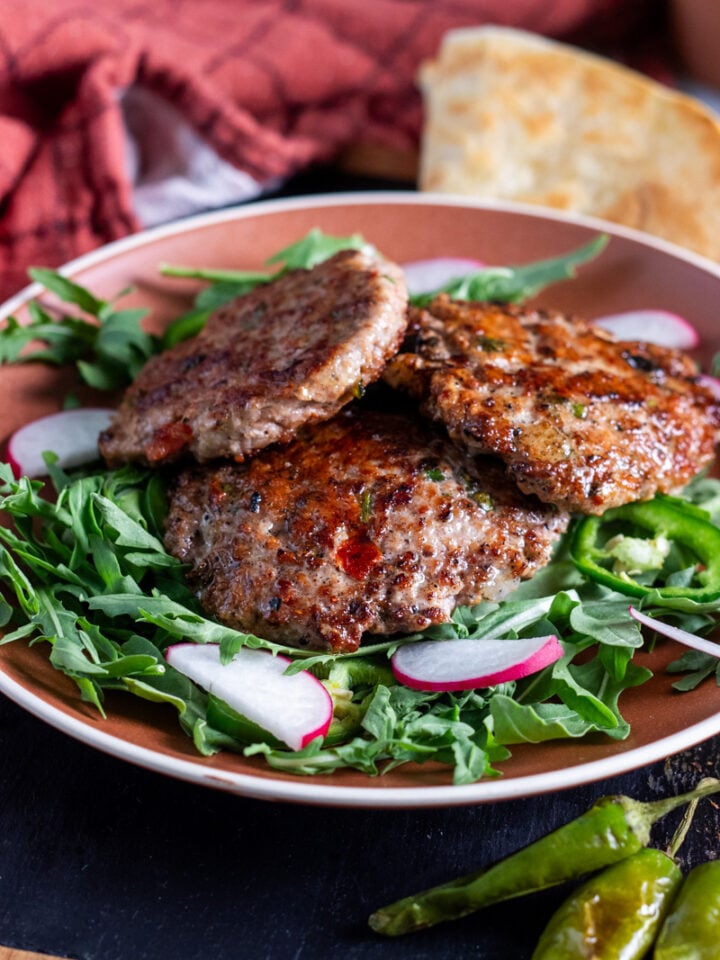 chicken chapli kabab on a bed or arugula, paratha in the back