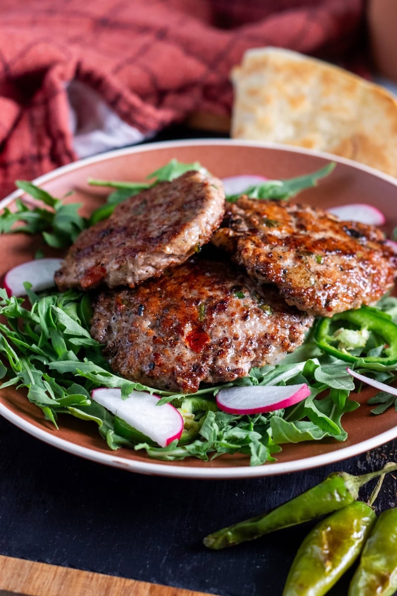 chicken chapli kabab on a bed or arugula, paratha in the back