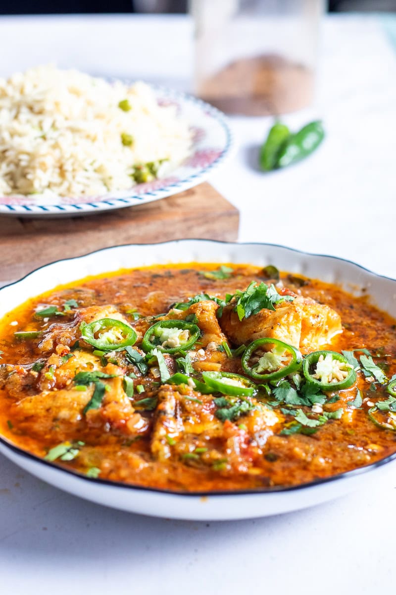 fish salan in a bowl, rice in the background
