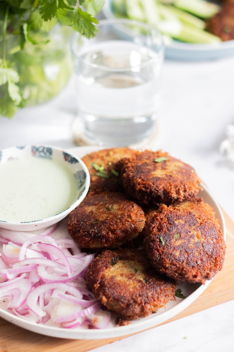 a plate of shami kabab with onions, a green raita/chutney and cilantro in a jar in the background