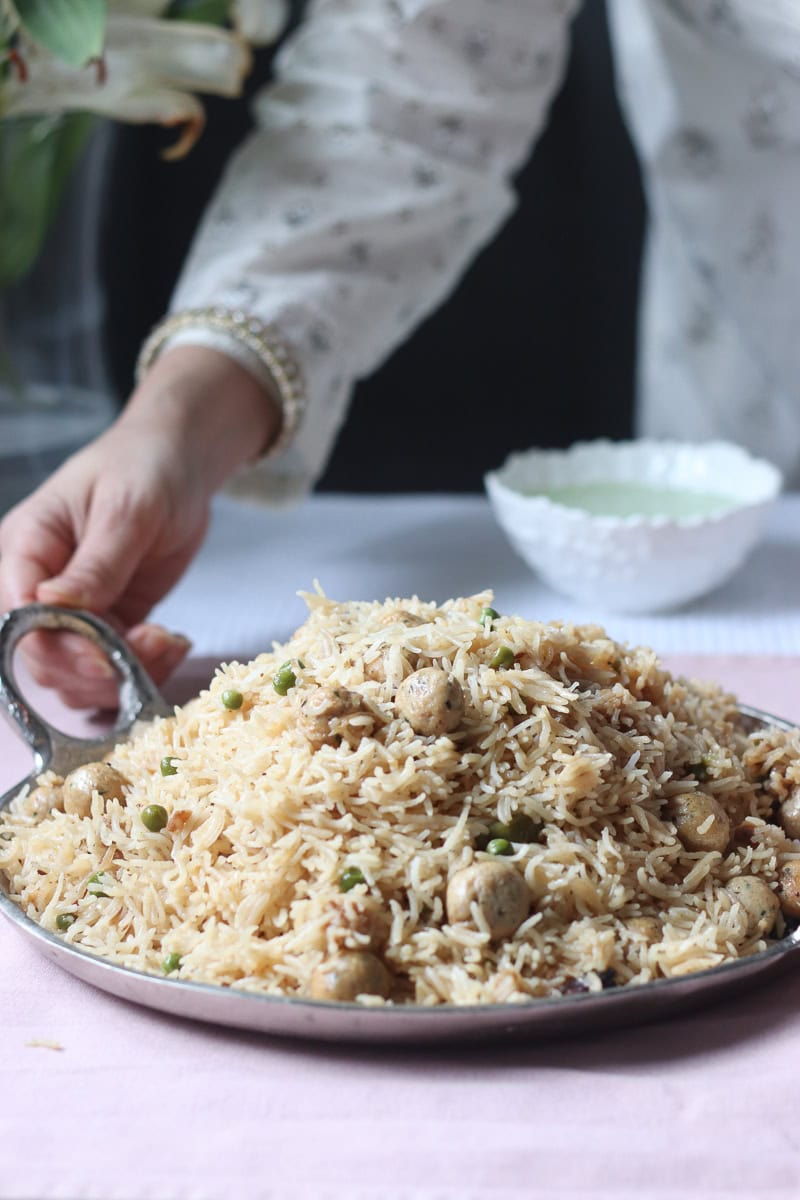 a person standing in the back holding a dish of moti pulao