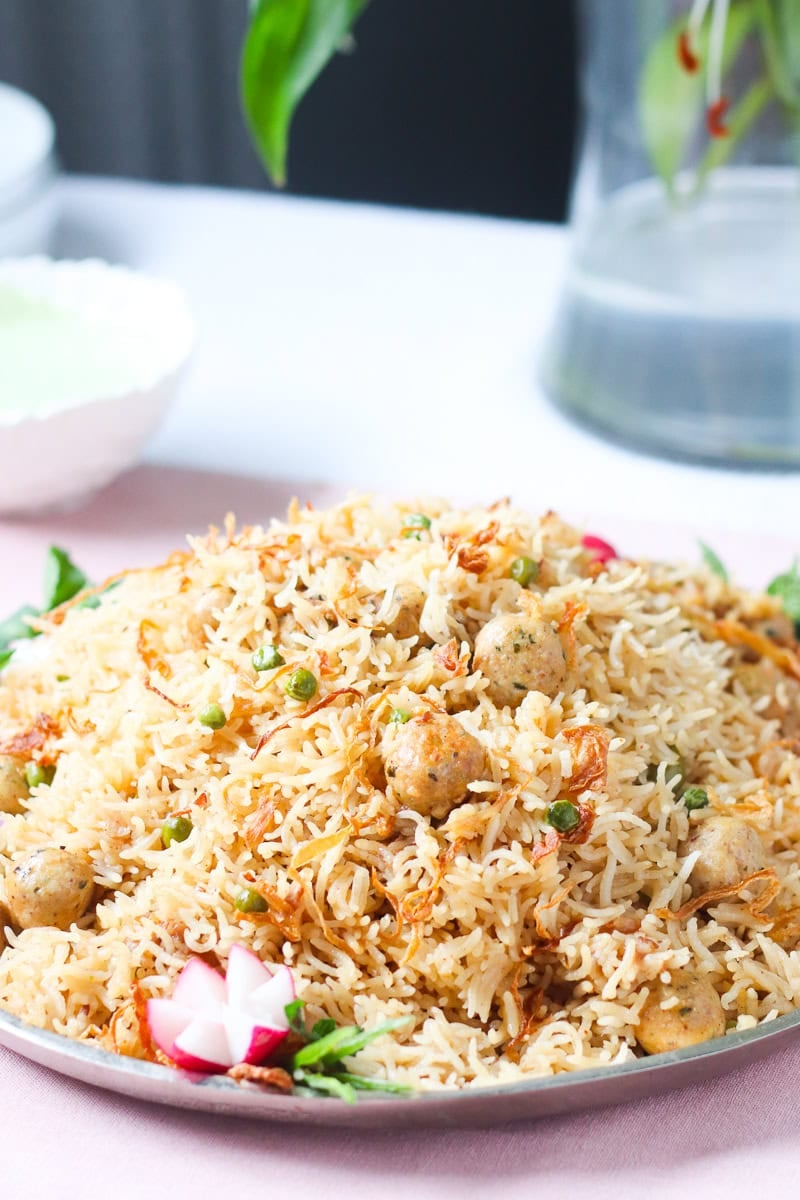 moti pulao on a silver handled platter with a bowl of green raita in the background