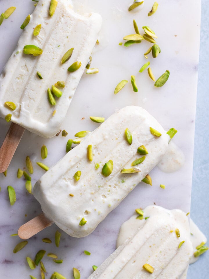 pista kulfi on a marble board with pistachios scattered over top